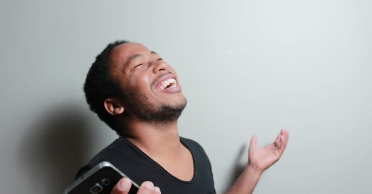 Airport Transfer Blogs | Articles | News | Tips & Tricks | Video | FAQ | Information | Infograph. 31 A cheerful man joyfully expresses happiness while holding a smartphone indoors.
