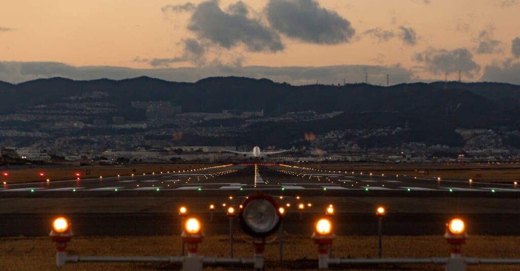 Scenic view of airplane landing on Osaka runway during dusk with city skyline.