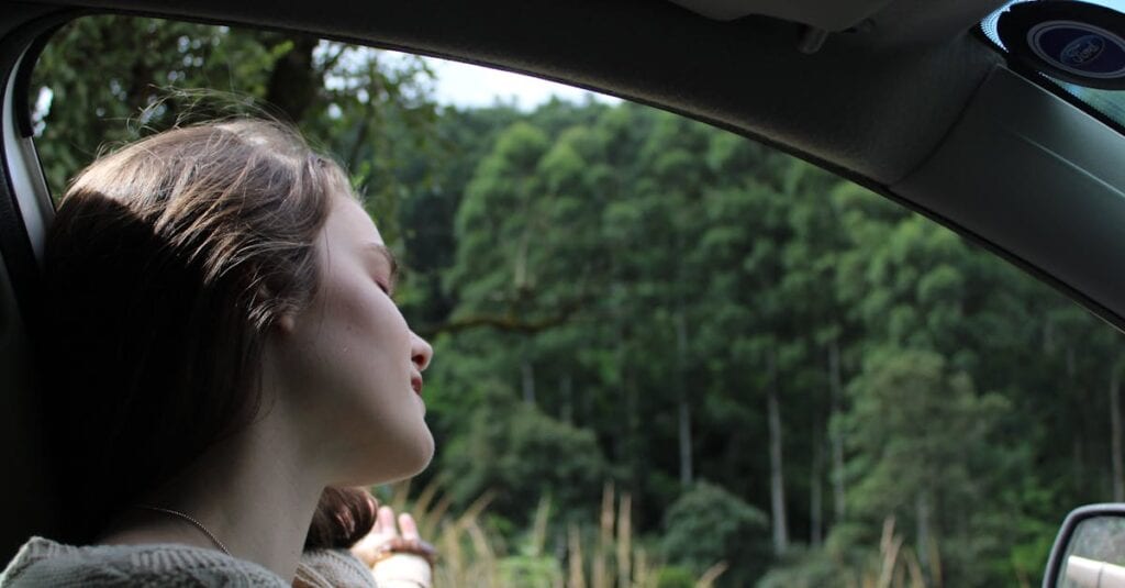 A young woman relaxes while enjoying a serene road trip surrounded by lush greenery.