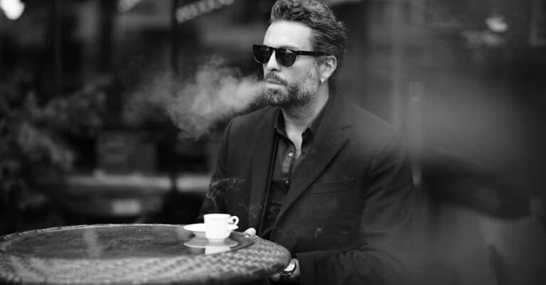Places & Attractions Blogs | Articles | News | Tips & Tricks | Video | FAQ | Information | Infograph. 9 Black and white photo of a well-dressed man smoking at a café, enjoying espresso.