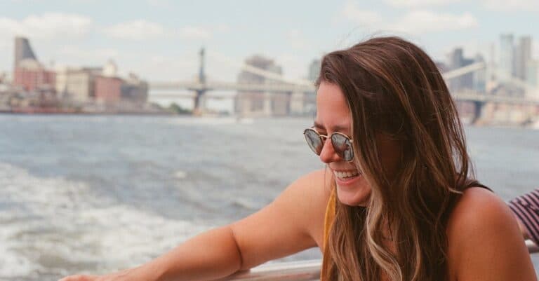 Car Service Blogs | Articles | News | Tips & Tricks | Video | FAQ | Information | Infograph. 4 Smiling woman in sunglasses enjoys a summertime boat ride with New York City skyline in the background.