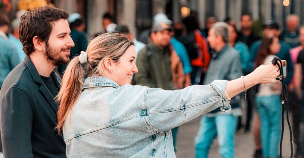 Young couple taking a selfie in a bustling street of Montréal, capturing the lively atmosphere.