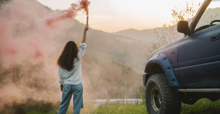 Places & Attractions Blogs | Articles | News | Tips & Tricks | Video | FAQ | Information | Infograph. 23 Woman with smoke flare and SUV in scenic mountain landscape at sunset.