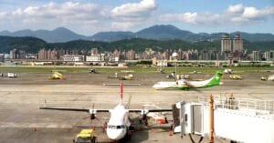 Aerial view of planes and tarmac at Songshan Airport in Taipei, Taiwan, with city skyline in background.