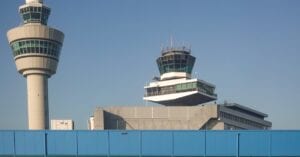 View of air traffic control towers at Amsterdam Schiphol Airport under clear blue sky.