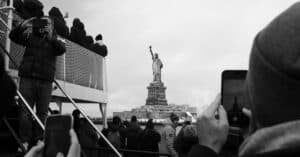 Black and white photo of tourists taking pictures of the Statue of Liberty from a New York City ferry.