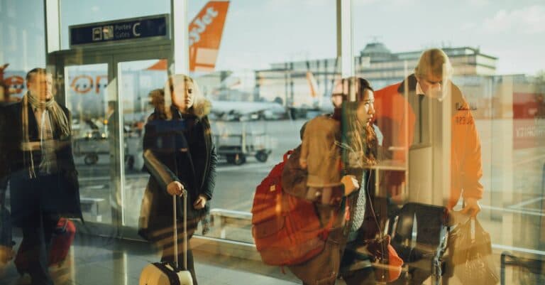 Places & Attractions Blogs | Articles | News | Tips & Tricks | Video | FAQ | Information | Infograph. 34 Passengers moving through an airport gate area with visible airplanes outside.