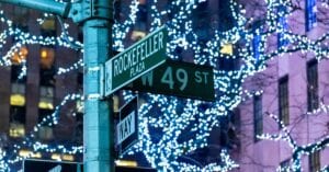 Street sign at Rockefeller Plaza adorned with festive lights in New York City at night.