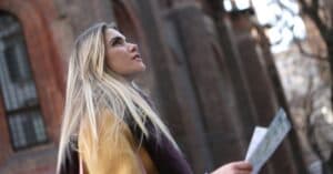 A young woman with long hair looks up while holding a map in an urban setting.