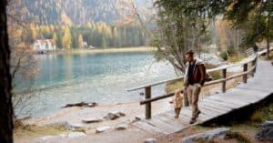 A father and child walk by a picturesque lake surrounded by autumn trees, capturing a moment of togetherness and adventure.