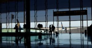 Travelers silhouetted in a modern airport terminal with glass windows and visible airplane tails.
