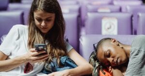Two young women relaxing in a station. One is texting while the other is resting.