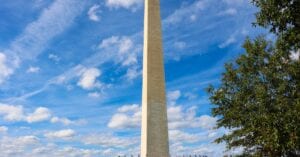 Stunning photo of the Washington Monument against a vibrant blue sky with clouds, surrounded by green grass.