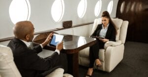Businessman and businesswoman in a private jet cabin working on digital devices.