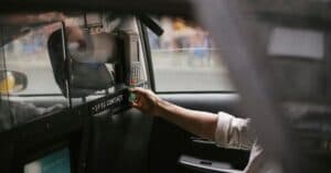 Side view of crop faceless male passenger sitting on backseat and using credit card reader to pay for trip in taxi