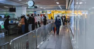 Travelers passing through airport security with staff and metal railings visible.
