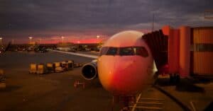 Plane boarding at sunset with vibrant sky colors and airport lights.
