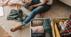 Woman organizing clothes while sitting on floor with open suitcase, preparing for a trip.