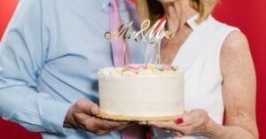 An elderly couple joyfully holding a 'Mr & Mrs' wedding anniversary cake.