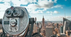 View of New York City skyline featuring iconic Empire State Building with observation binoculars in the foreground.