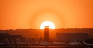 Vibrant sunset at San Bernardino Airport with airplanes and air traffic control tower silhouetted against the orange horizon.
