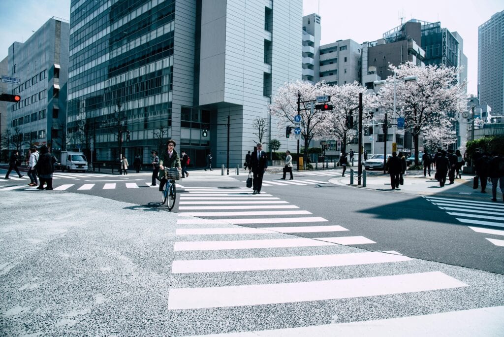 Pedestrians crossing a busy intersection in Nagawa, Japan with cherry blossoms and modern architecture.