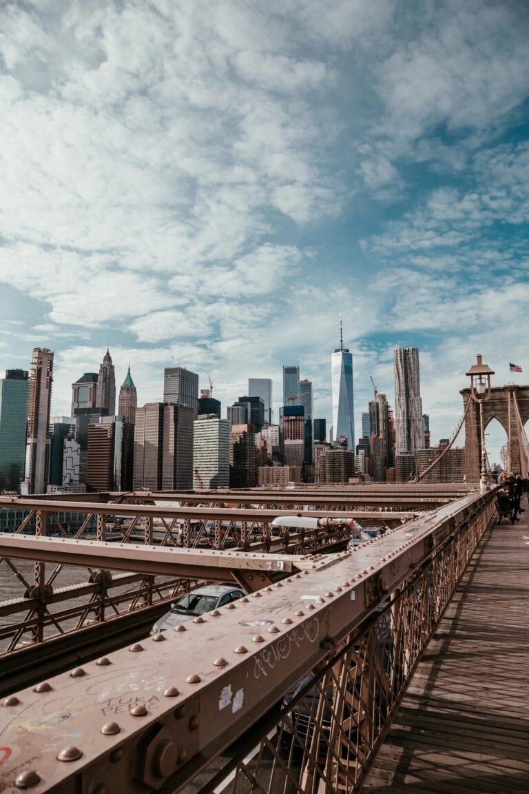 A breathtaking view of the New York City skyline from the Brooklyn Bridge, featuring iconic skyscrapers under a cloudy sky.