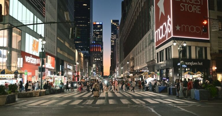 Evening scene at a busy New York intersection with pedestrians and neon lights.