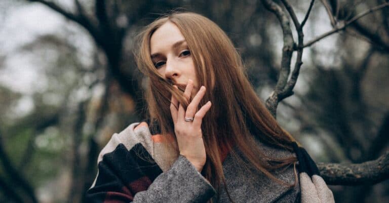 Portrait of a thoughtful woman in a grey coat amidst bare trees.