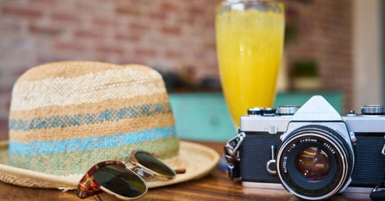 A stylish scene showcasing a vintage camera, hat, and orange juice, evoking summer travel vibes.