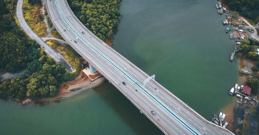 Drone view of a serene bridge crossing over a lush green river amidst vibrant foliage.