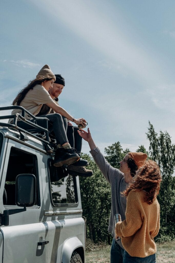 Group of friends enjoying a summer road trip with an SUV, relaxing outdoors and having fun.