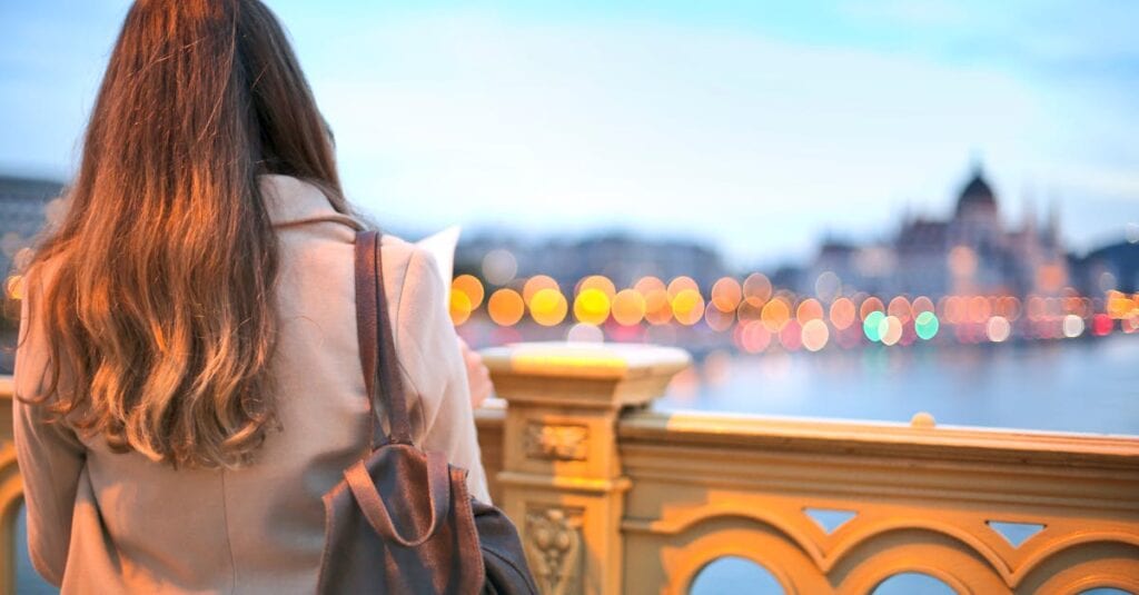A woman enjoys a scenic view of Budapest's Danube River with bokeh lights in the background.