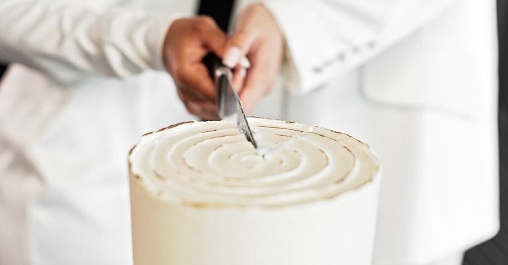 Close-up of couple cutting a simple white wedding cake with a knife.