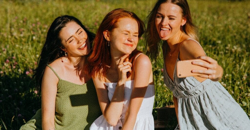 Three young women enjoying a cheerful selfie outdoors in a sunny park, capturing fun and friendship.