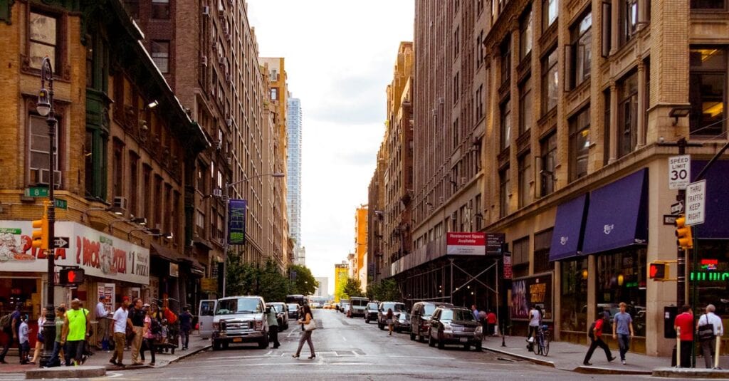 Lively urban street in New York City with pedestrians and vehicles on a sunny day.