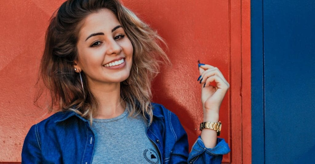 A woman in a denim jacket smiling brightly against a vibrant red and blue background.