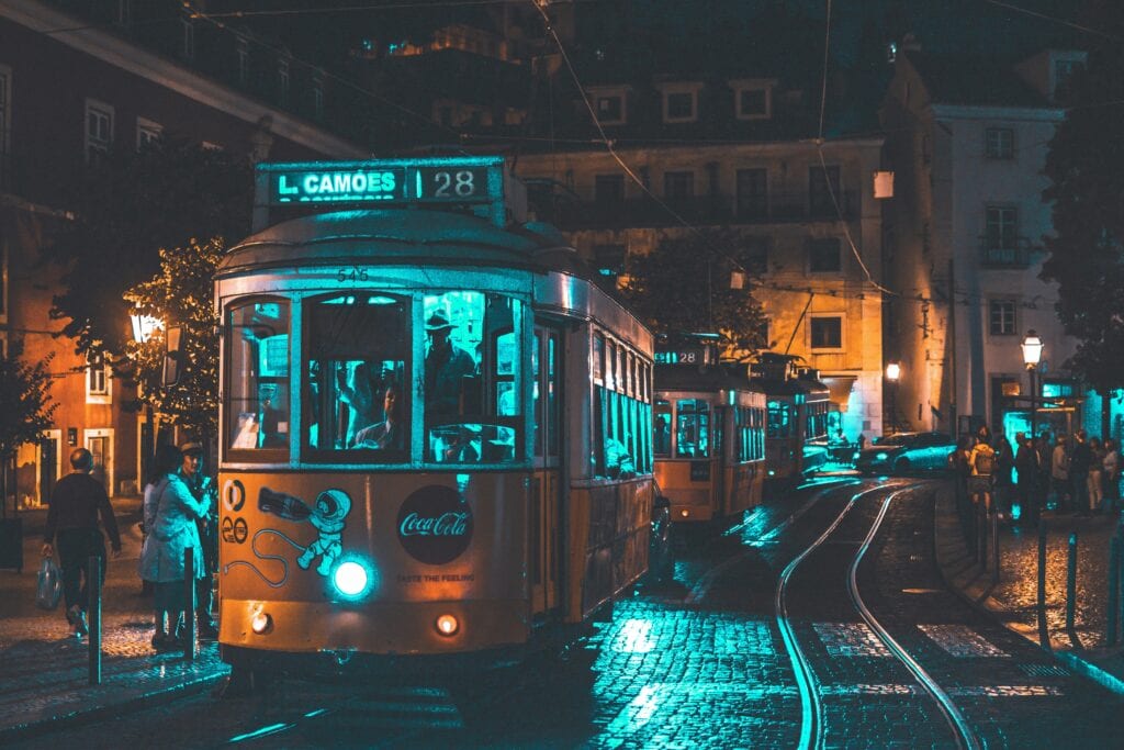 Illuminated vintage tram rides through Lisbon at night showcasing urban life and street lighting ambiance.