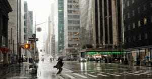 Street scene in New York City with people and umbrellas during rain, reflecting urban life.