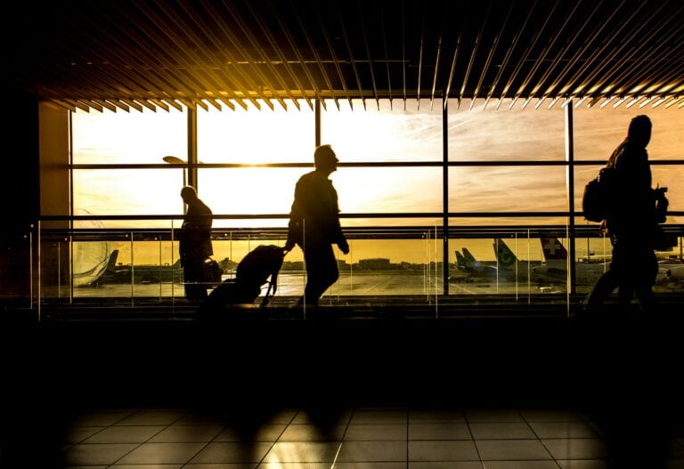 Travelers in silhouette pulling luggage at the airport during a beautiful sunset.