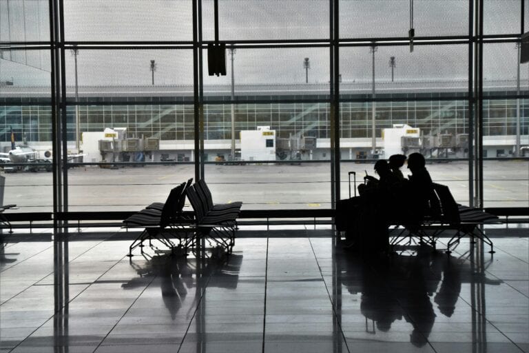 Silhouette of unrecognizable passengers sitting on chairs with luggage near window and waiting for flight
