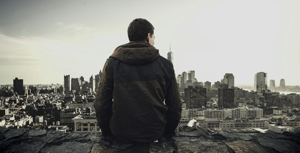 Man sitting on rooftop overlooking city skyline, contemplating the urban landscape.