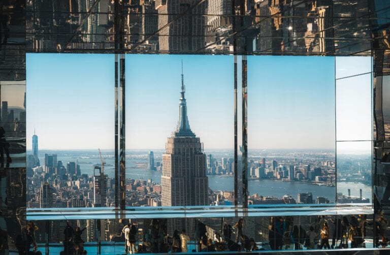An aerial view of the Empire State Building through reflective glass, capturing New York City's iconic skyline.
