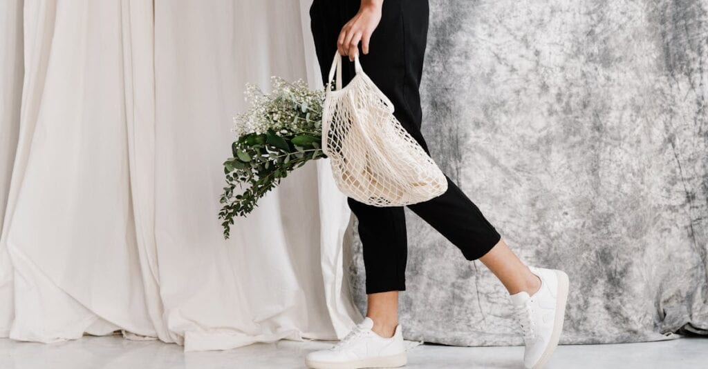 Woman in minimalist outfit holding an eco-friendly mesh bag filled with flowers, showcasing sustainable fashion.