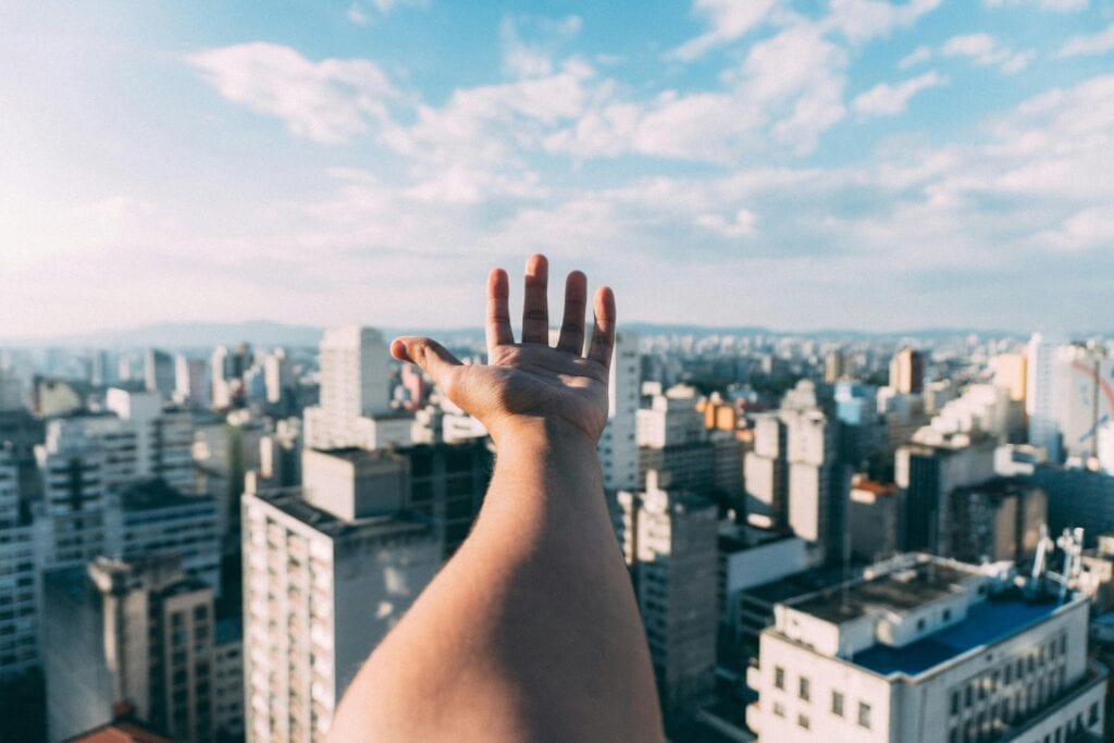 An outstretched hand reaching towards a sunny cityscape, capturing the vibrant skyline and skyscrapers.