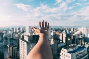 An outstretched hand reaching towards a sunny cityscape, capturing the vibrant skyline and skyscrapers.