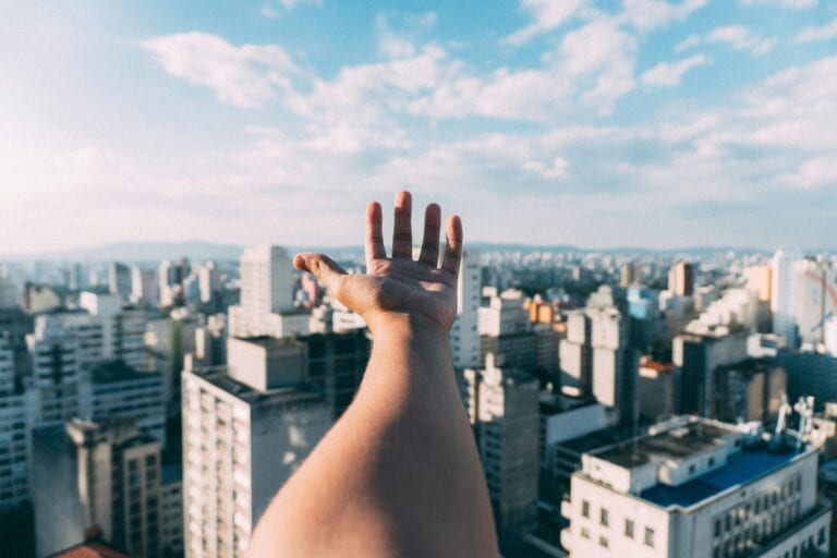 An outstretched hand reaching towards a sunny cityscape, capturing the vibrant skyline and skyscrapers.