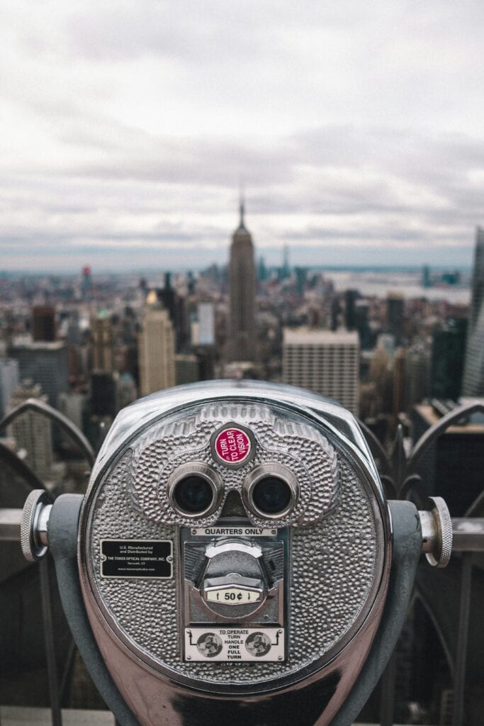 Binocular viewer focusing on New York City skyline featuring Empire State Building on a cloudy day.