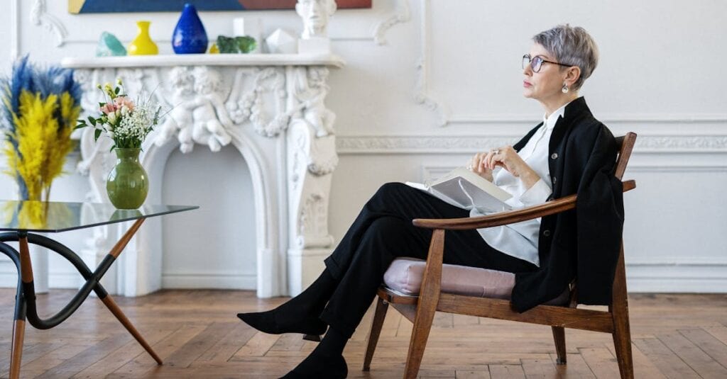 A mature woman sits pensively in a chic interior, embodying elegance and tranquility.