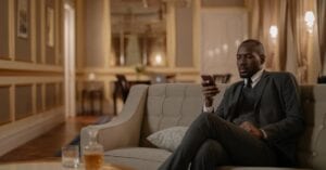 Elegant businessman using smartphone while relaxing in hotel lounge with whiskey on the table.